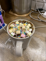 A christmassy mug cake with pink icing, unicorn sprinkles, and marshmallow decorations